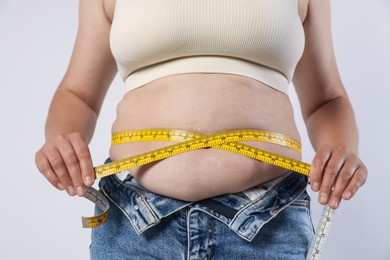Photo of Overweight woman measuring her belly with tape on light background, closeup