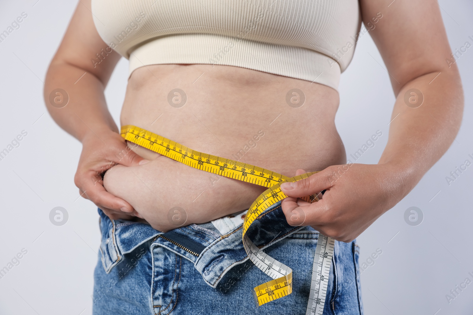 Overweight woman measuring her belly with tape on light background, closeup Photo of Overweight woman measuring her belly with tape on light background, closeup