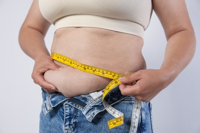 Photo of Overweight woman measuring her belly with tape on light background, closeup