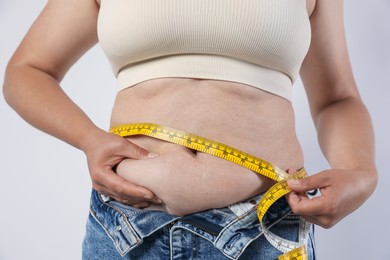 Photo of Overweight woman measuring her belly with tape on light background, closeup