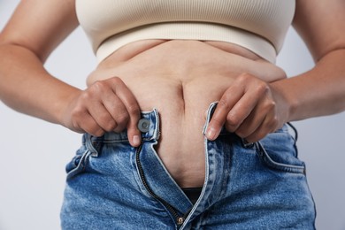 Photo of Overweight woman trying to put on tight jeans against light background, closeup