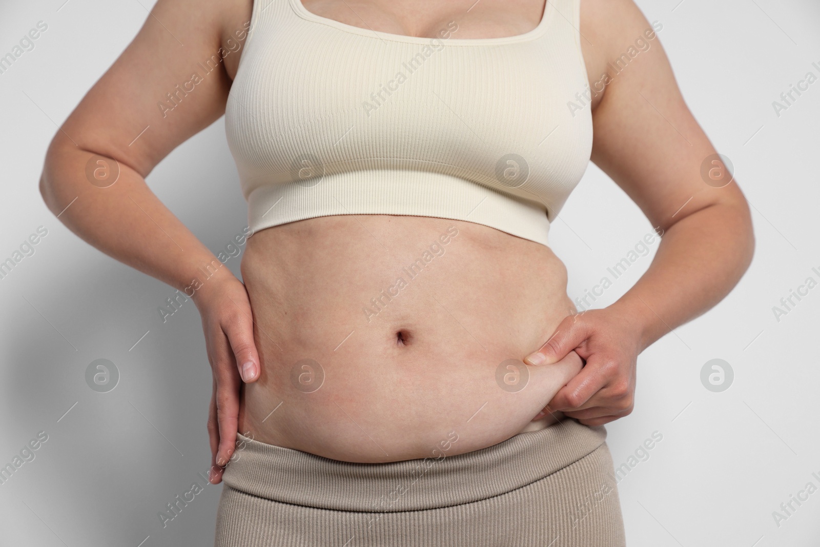 Photo of Woman with excessive belly fat on light background, closeup. Overweight problem