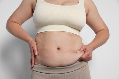 Photo of Woman with excessive belly fat on light background, closeup. Overweight problem