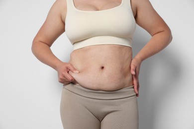 Photo of Woman with excessive belly fat on light background, closeup. Overweight problem