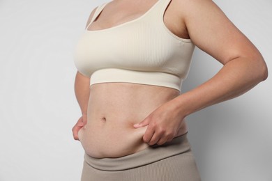 Photo of Woman with excessive belly fat on light background, closeup. Overweight problem