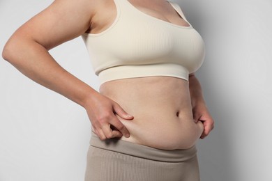 Photo of Woman with excessive belly fat on light background, closeup. Overweight problem
