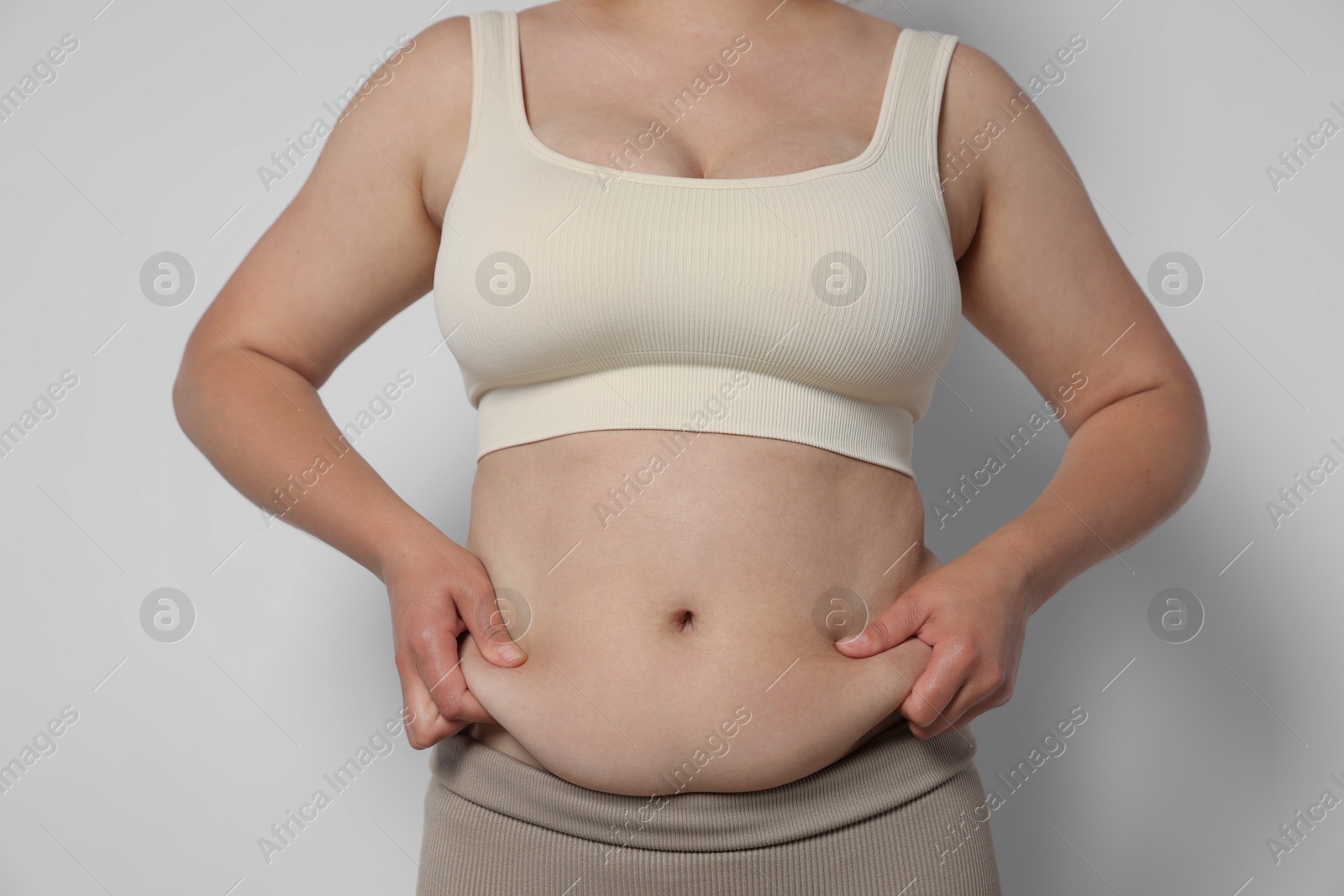 Woman with excessive belly fat on light background, closeup. Overweight problem Photo of Woman with excessive belly fat on light background, closeup. Overweight problem