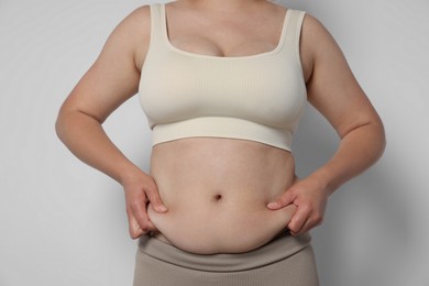 Photo of Woman with excessive belly fat on light background, closeup. Overweight problem