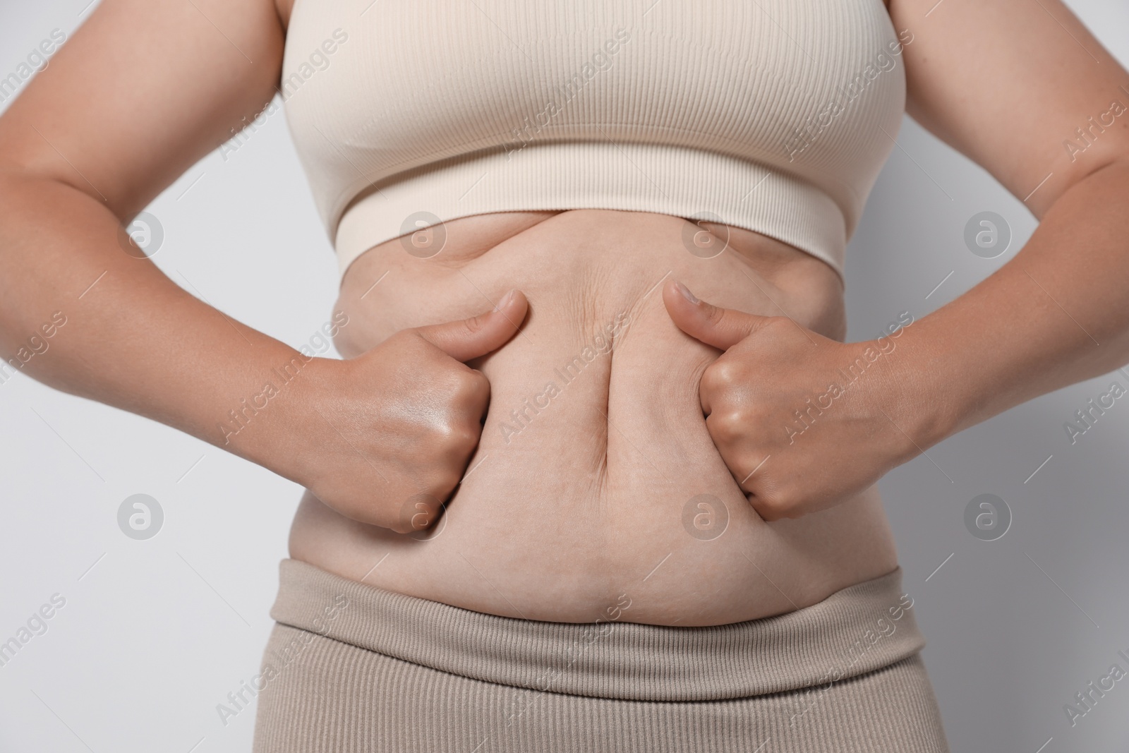 Woman with excessive belly fat on light background, closeup. Overweight problem Photo of Woman with excessive belly fat on light background, closeup. Overweight problem