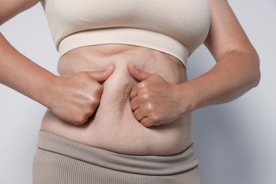 Photo of Woman with excessive belly fat on light background, closeup. Overweight problem