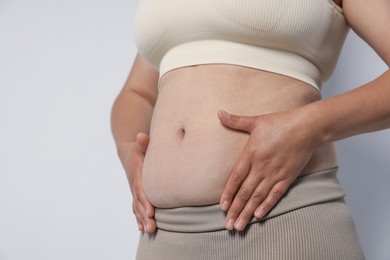 Photo of Woman with excessive belly fat on light background, closeup. Overweight problem