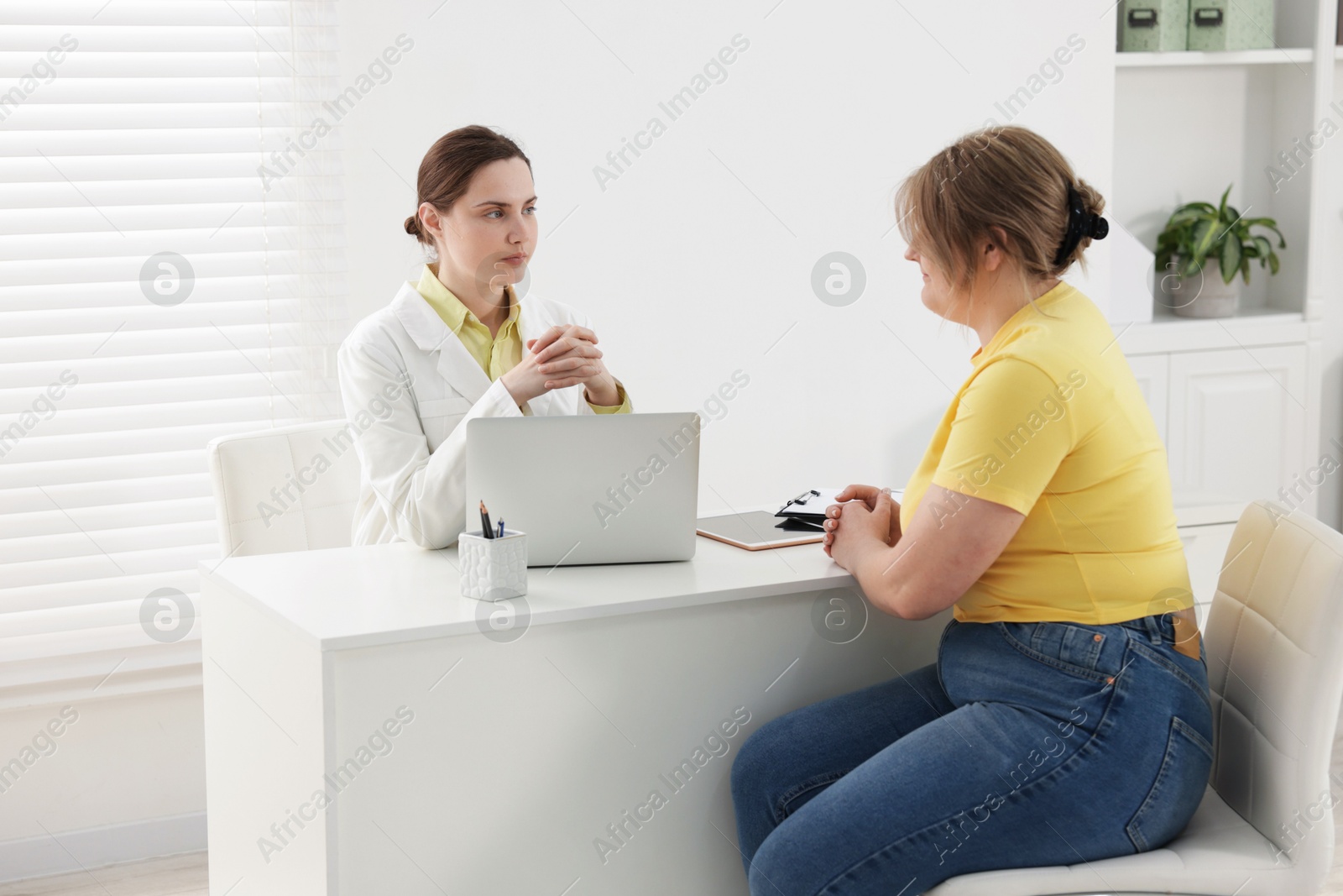 Weight loss. Nutritionist consulting overweight woman at white desk in clinic Photo of Weight loss. Nutritionist consulting overweight woman at white desk in clinic