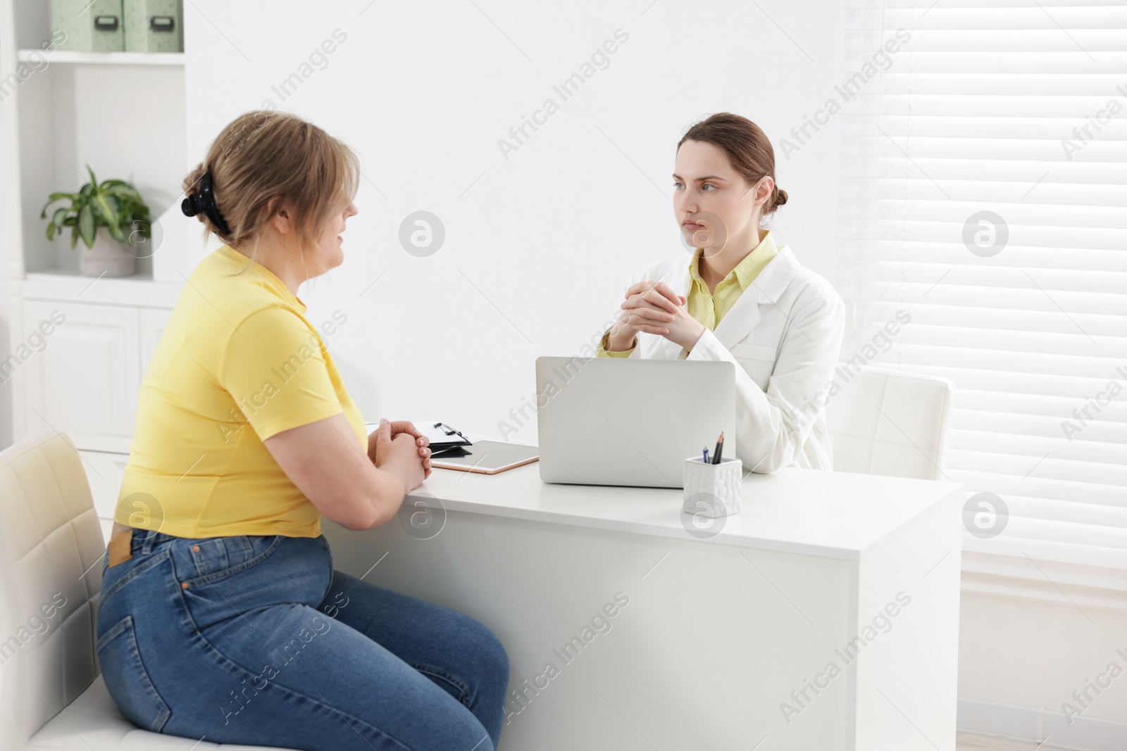 Weight loss. Nutritionist consulting overweight woman at white desk in clinic Photo of Weight loss. Nutritionist consulting overweight woman at white desk in clinic