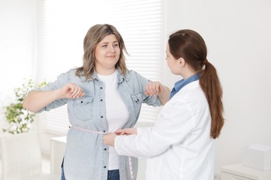Photo of Weight loss. Nutritionist measuring happy overweight woman's waist with tape in clinic