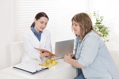 Photo of Weight loss. Nutritionist consulting overweight woman at white desk in clinic