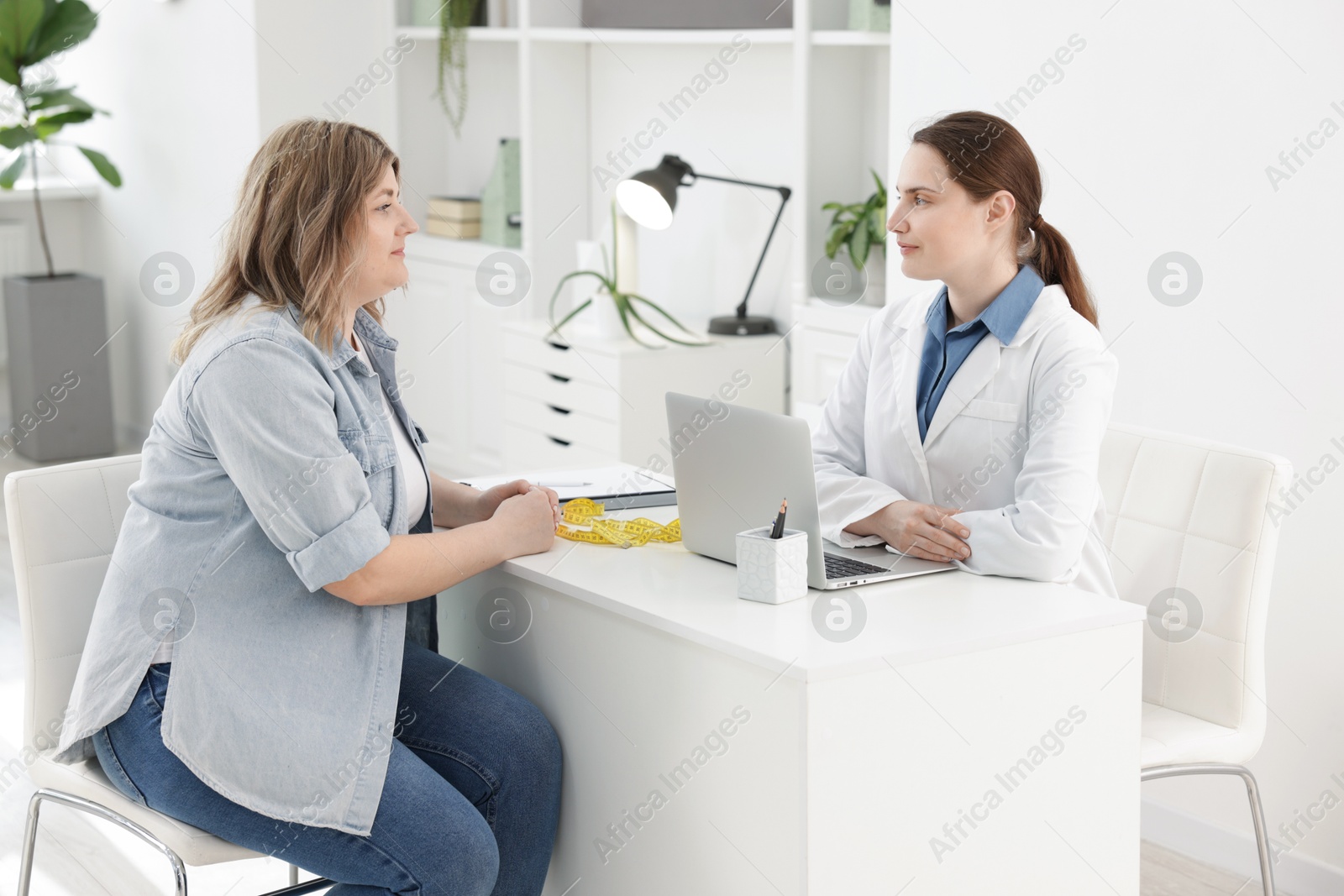 Weight loss. Nutritionist consulting overweight woman at white desk in clinic Photo of Weight loss. Nutritionist consulting overweight woman at white desk in clinic
