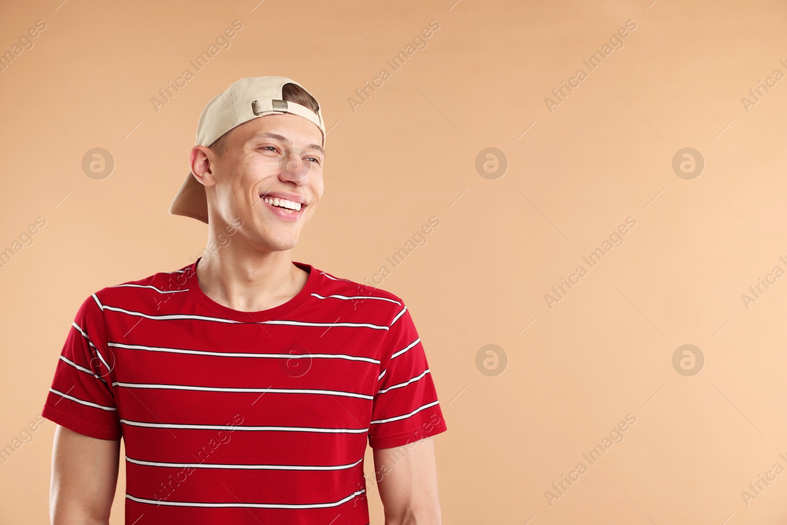 Young man in stylish baseball hat on beige background, space for text Photo of Young man in stylish baseball hat on beige background, space for text