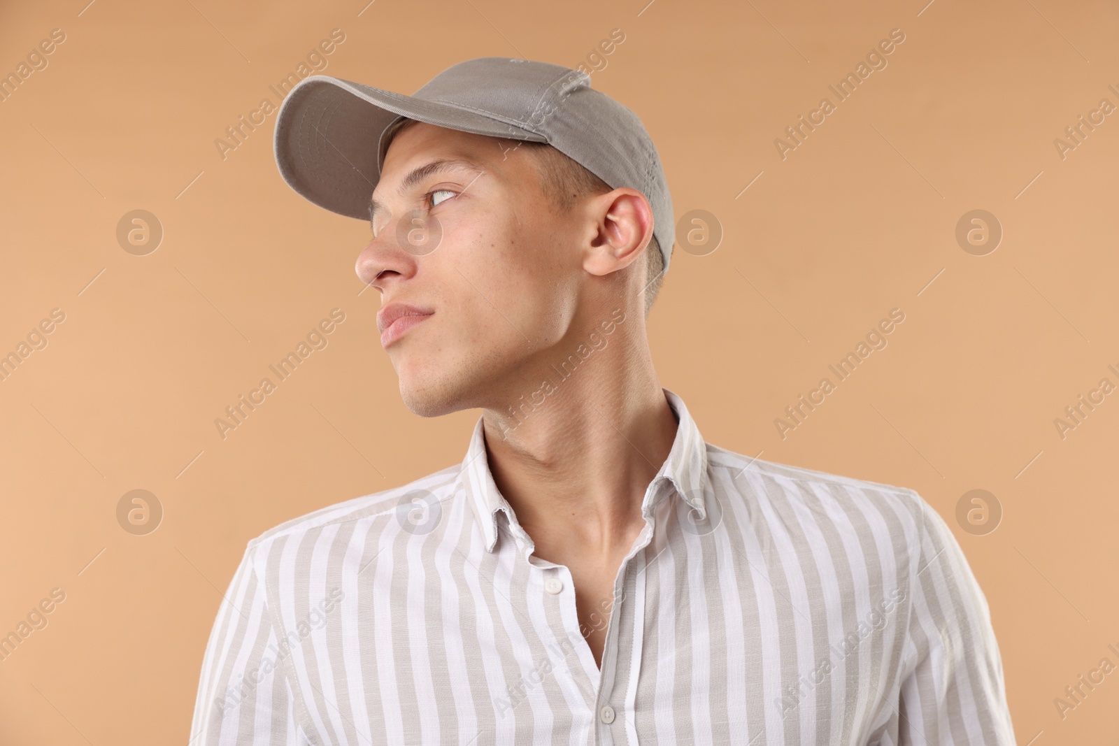 Young man in stylish baseball hat on beige background Photo of Young man in stylish baseball hat on beige background