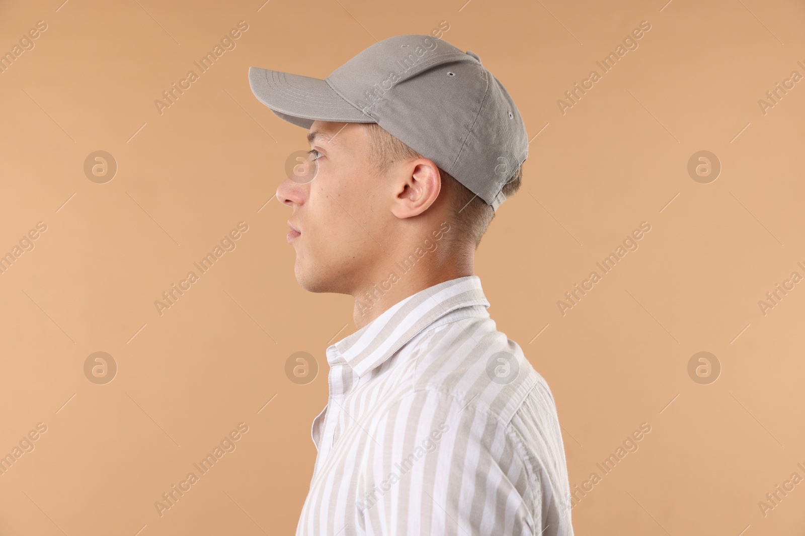 Young man in stylish baseball hat on beige background Photo of Young man in stylish baseball hat on beige background