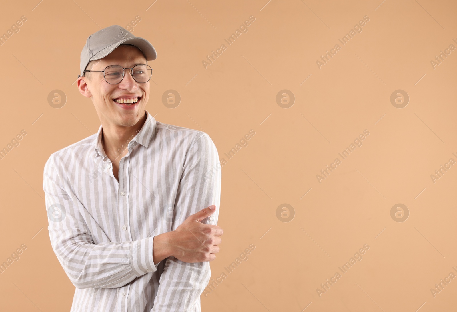 Young man in stylish baseball hat on beige background, space for text Photo of Young man in stylish baseball hat on beige background, space for text