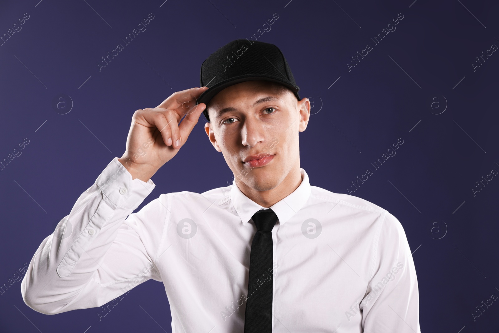 Young man in stylish baseball hat on dark blue background Photo of Young man in stylish baseball hat on dark blue background