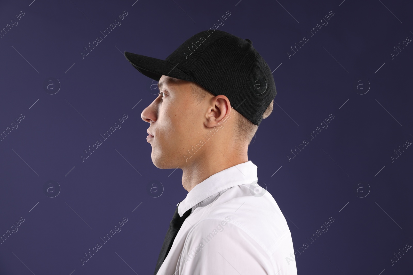 Young man in stylish baseball hat on dark blue background Photo of Young man in stylish baseball hat on dark blue background