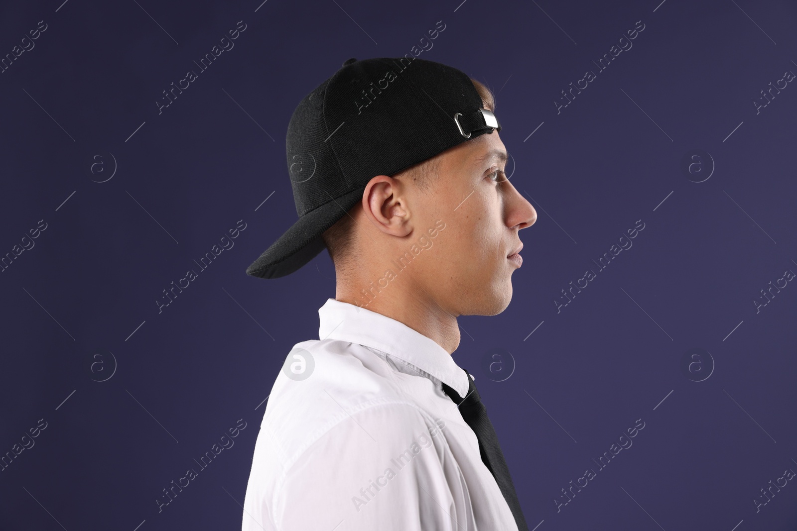 Young man in stylish baseball hat on dark blue background Photo of Young man in stylish baseball hat on dark blue background