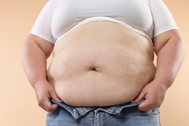 Photo of Woman with excessive belly fat on beige background, closeup