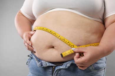 Photo of Overweight woman measuring her belly with tape on grey background, closeup