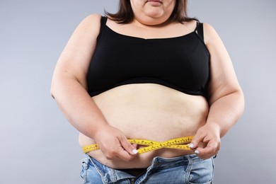 Photo of Overweight woman measuring her belly with tape on grey background, closeup