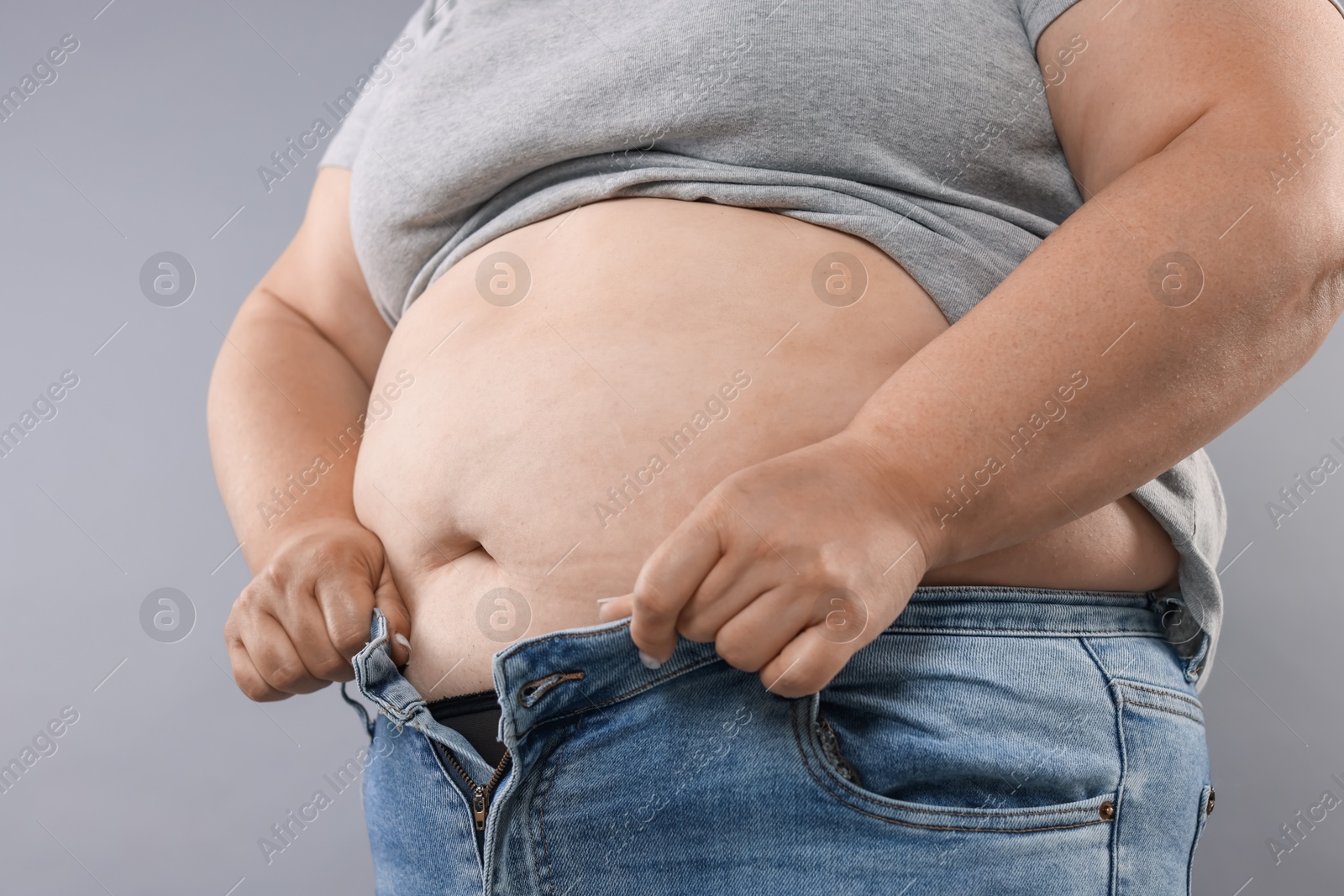 Overweight woman trying to put on tight jeans against grey background, closeup Photo of Overweight woman trying to put on tight jeans against grey background, closeup