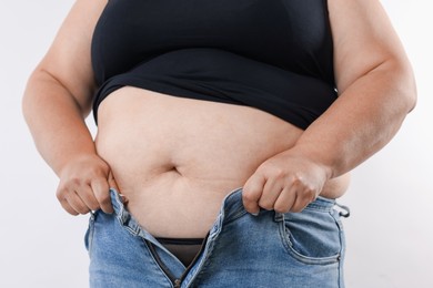Photo of Overweight woman trying to put on tight jeans against white background, closeup