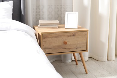 Photo of Bedside table with books and frame near bed indoors