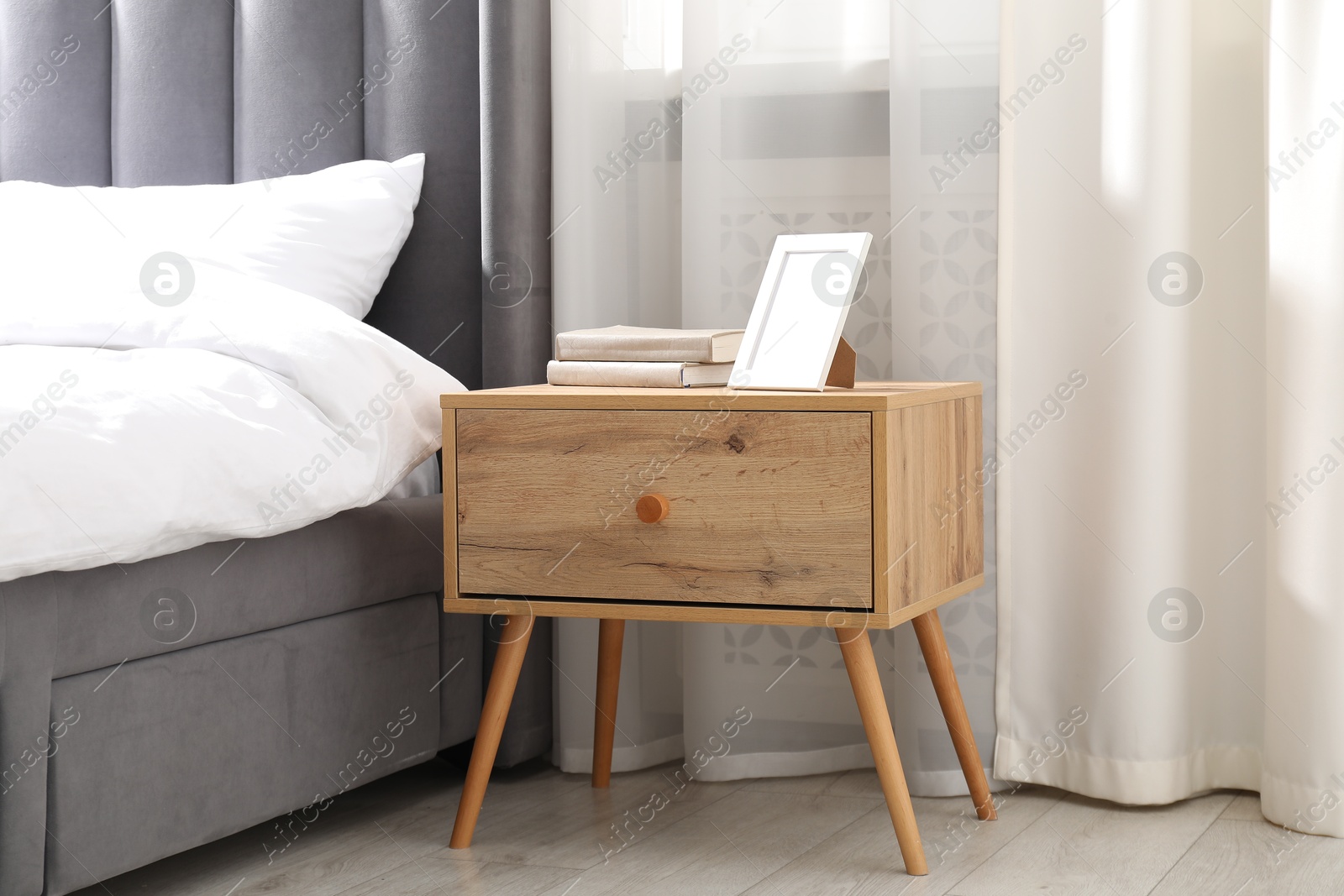 Bedside table with books and frame near bed indoors Photo of Bedside table with books and frame near bed indoors