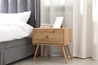 Photo of Bedside table with books and frame near bed indoors