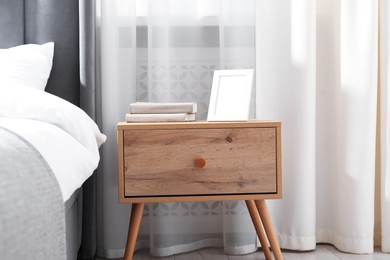 Photo of Bedside table with books and frame near bed indoors