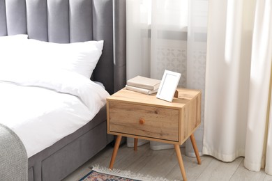 Photo of Bedside table with books and frame near bed indoors