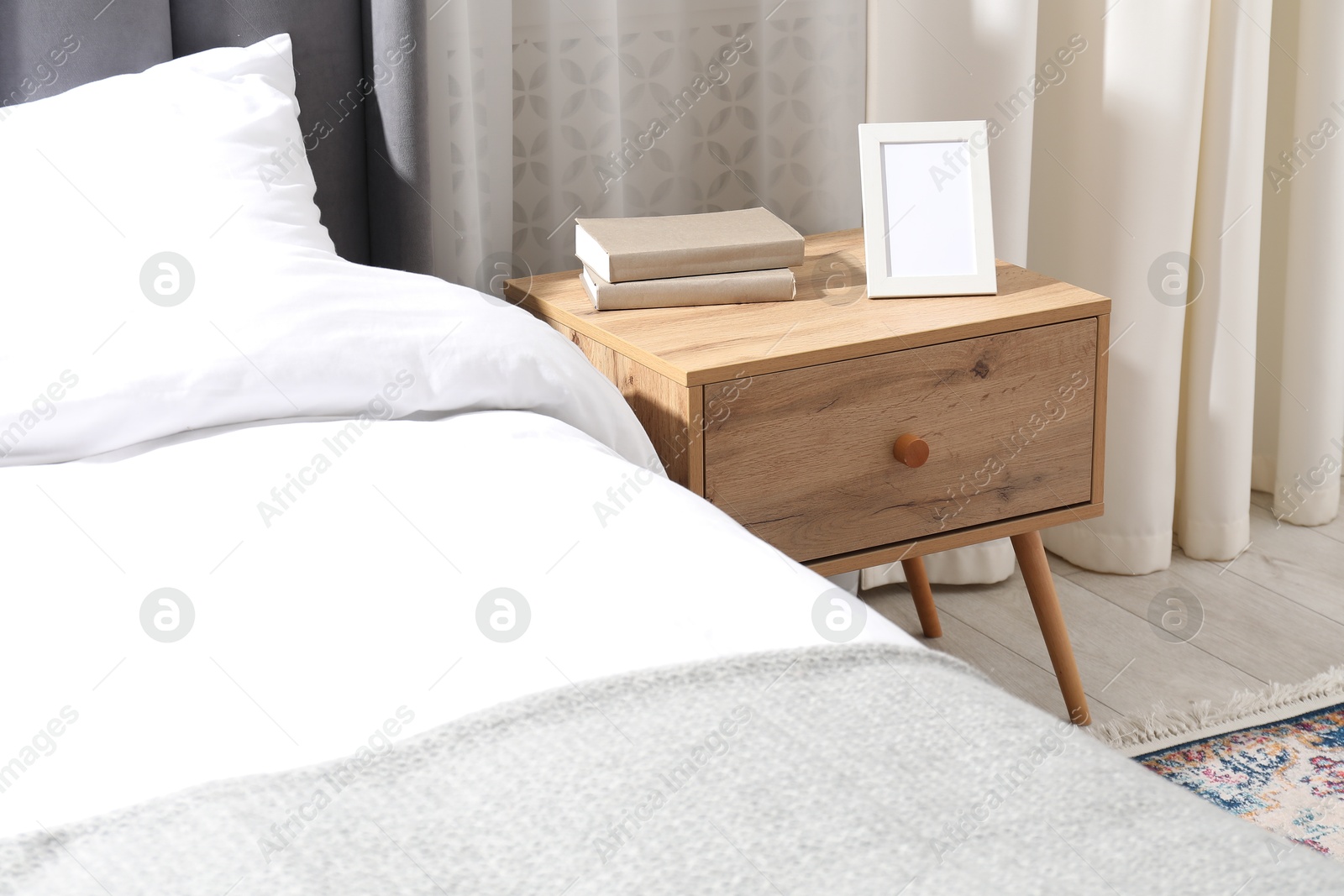 Bedside table with books and frame near bed indoors Photo of Bedside table with books and frame near bed indoors