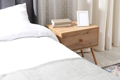 Photo of Bedside table with books and frame near bed indoors