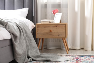 Photo of Bedside table with books, flower and frame near bed indoors