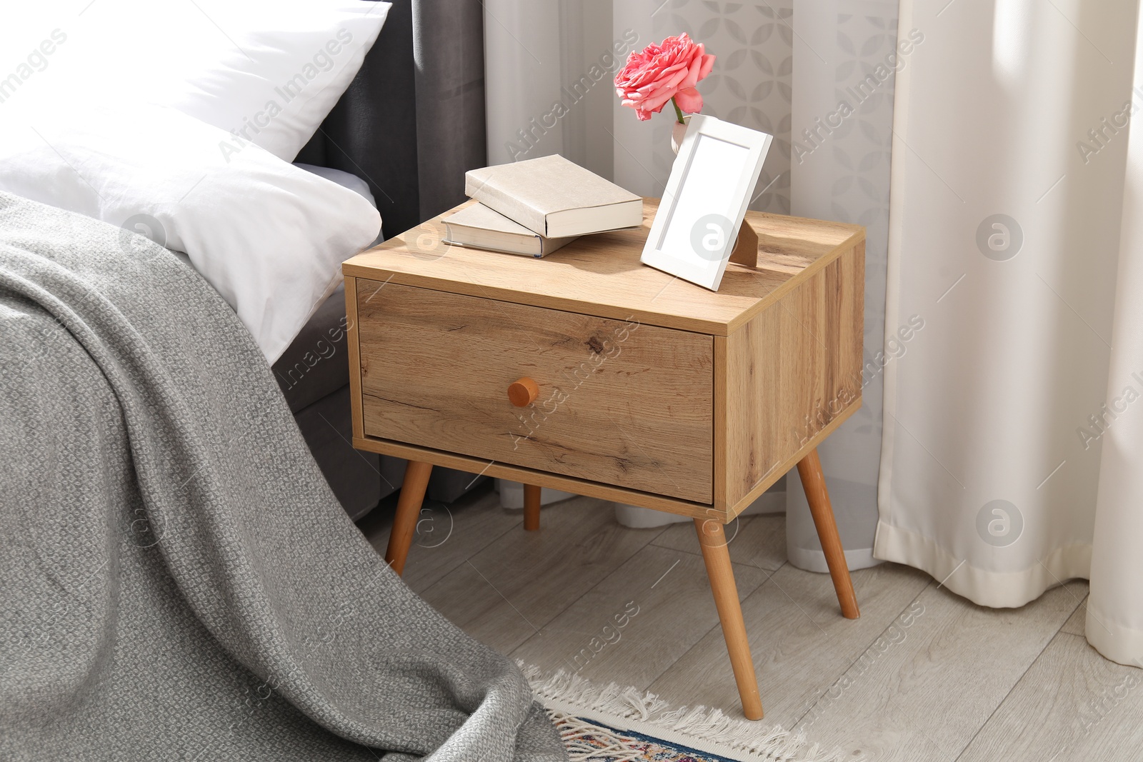 Bedside table with books, flower and frame near bed indoors Photo of Bedside table with books, flower and frame near bed indoors