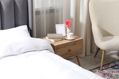 Photo of Bedside table with coffee, books and decor near bed indoors
