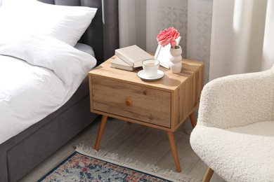 Photo of Bedside table with coffee, books and decor near bed indoors