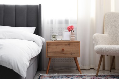 Photo of Bedside table with coffee, flower and alarm clock near bed indoors