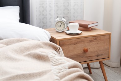 Photo of Bedside table with coffee, books and alarm clock near bed indoors