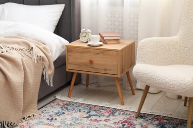 Photo of Bedside table with coffee, books and alarm clock near bed indoors