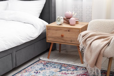 Photo of Bedside table with alarm clock and decor near bed indoors