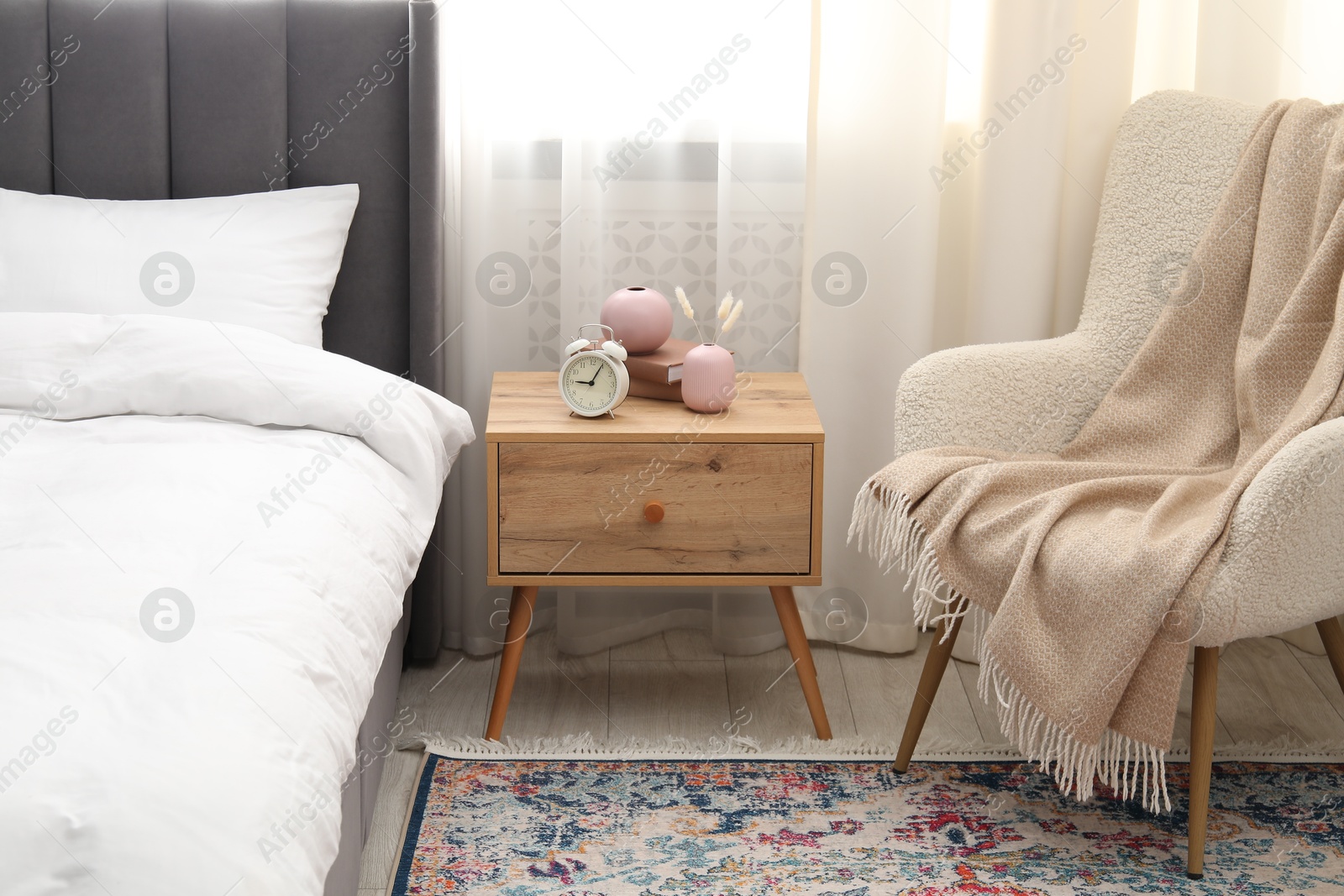 Bedside table with alarm clock and decor near bed indoors Photo of Bedside table with alarm clock and decor near bed indoors