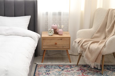 Photo of Bedside table with alarm clock and decor near bed indoors