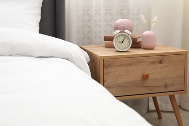 Photo of Bedside table with alarm clock and decor near bed indoors
